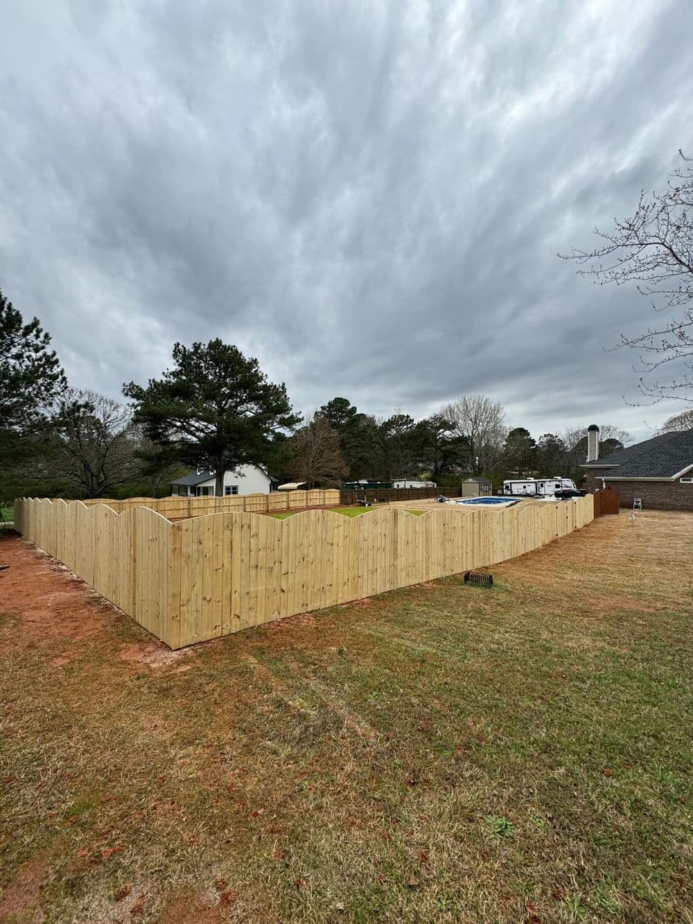 Wooden privacy fence surrounding a grassy yard under a cloudy sky.