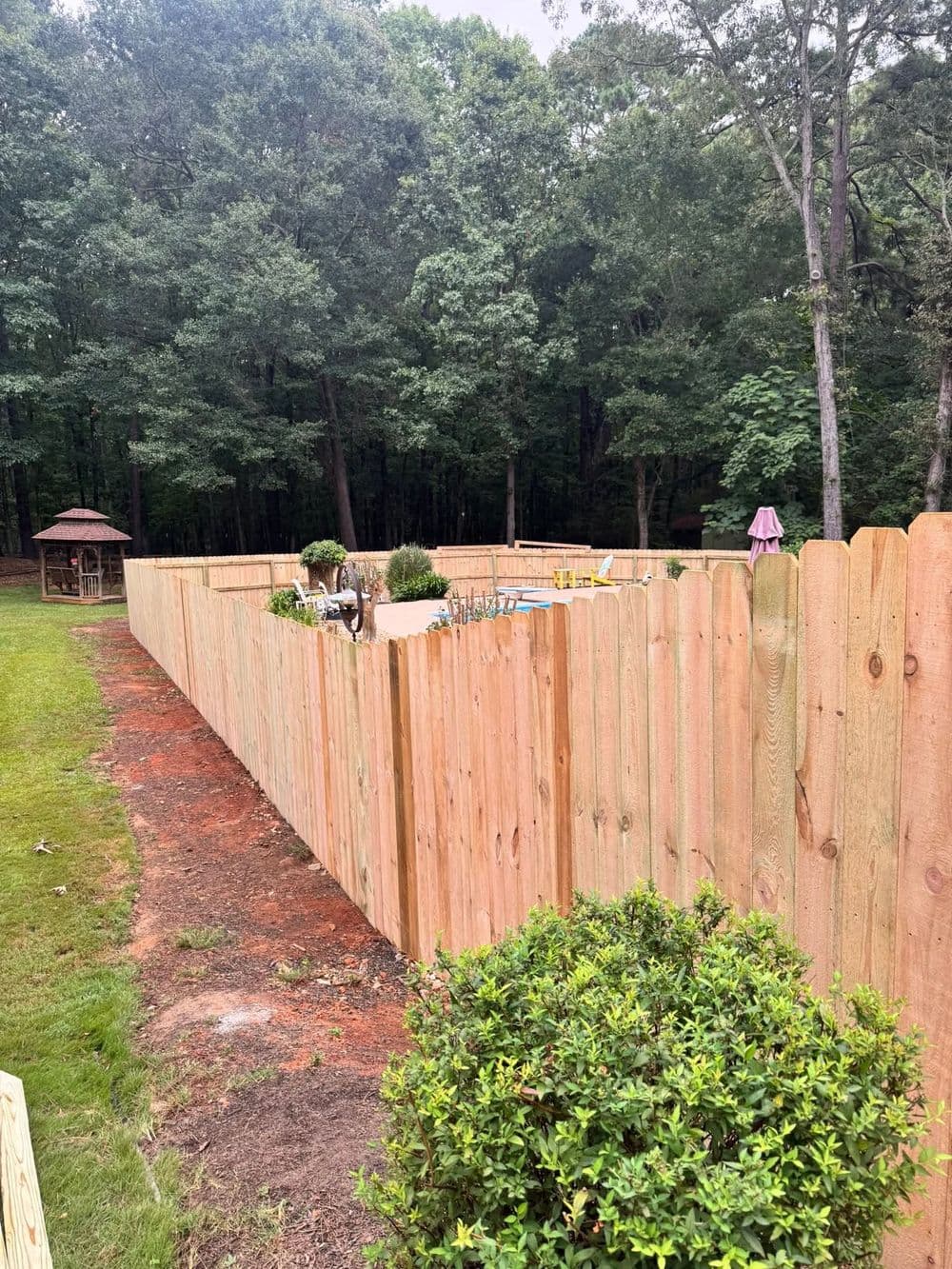 Wooden fence enclosing a pool area in a wooded backyard with landscaping.