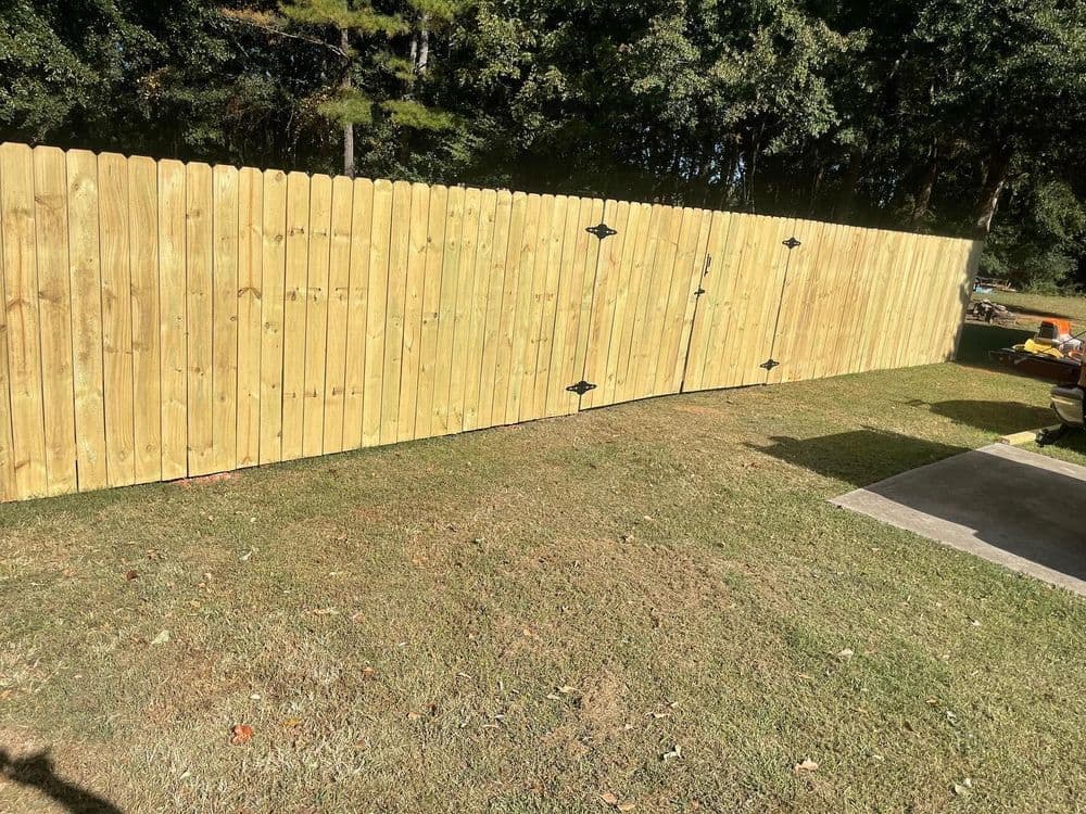 Wooden privacy fence with decorative hardware in a grassy backyard setting.