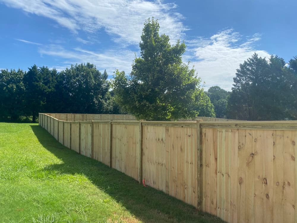 Wooden privacy fence surrounding a green lawn under a blue sky with scattered clouds.