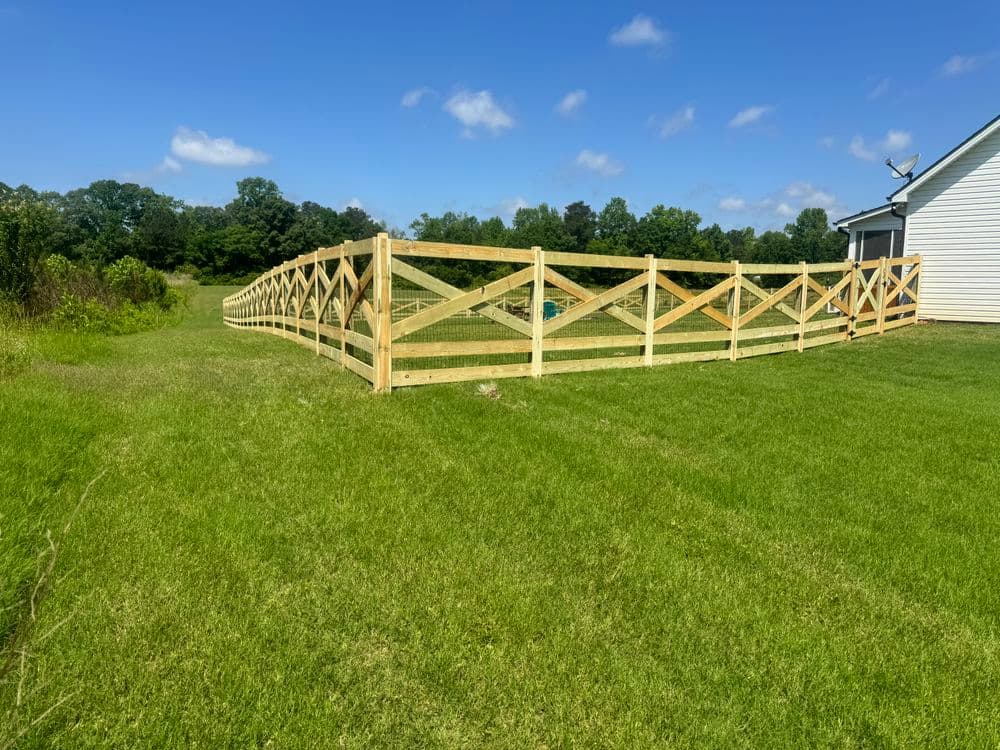 Wooden fence curving along green lawn with blue sky in background. Bright daylight scene.
