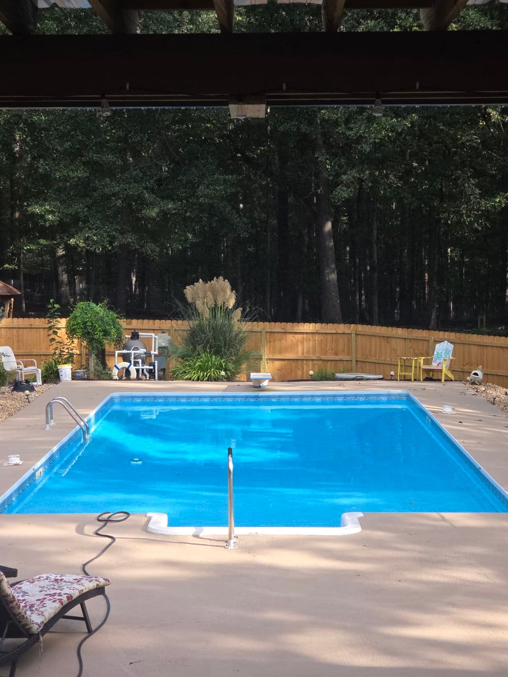 Blue swimming pool surrounded by a wooden fence and lush greenery in a serene backyard setting.