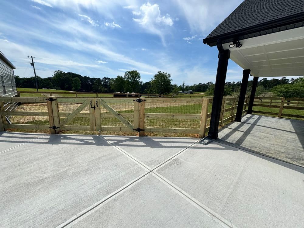 Newly constructed fence surrounding open field with clear blue sky and modern patio area.