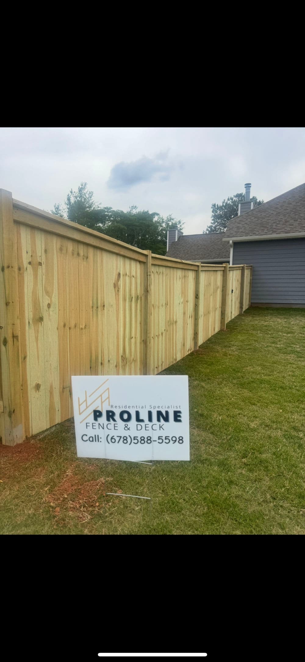 Wooden fence installation by ProLine Fence & Deck with contact information on display.