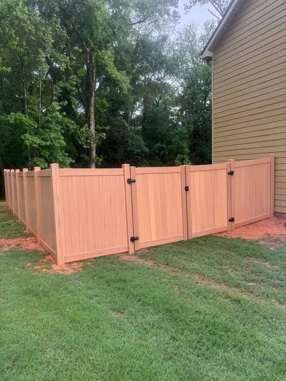 Wooden privacy fence in backyard with green grass and wooded area in the background.