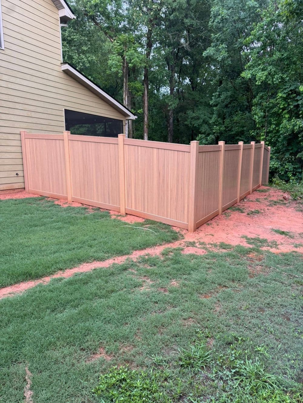 Wooden privacy fence in backyard with grass and trees in the background.