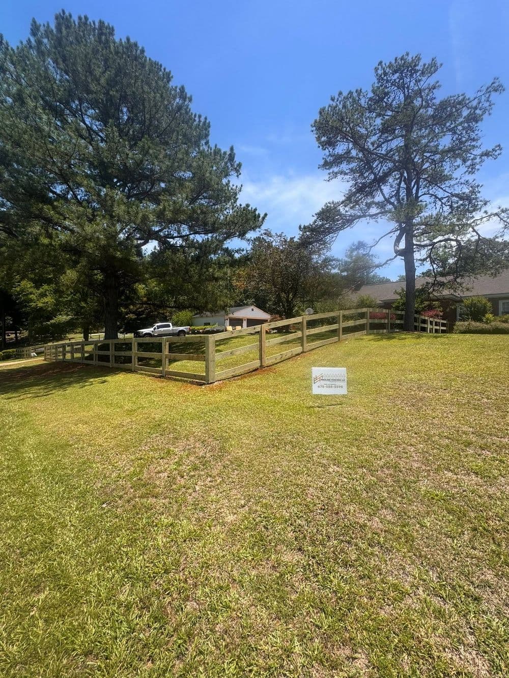 Fenced property with grassy area and trees under a clear blue sky.