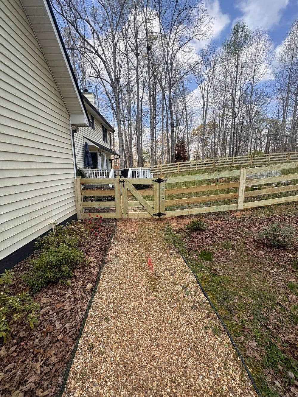 Pathway leading to a wooden gate and fenced yard, surrounded by trees and landscaping.