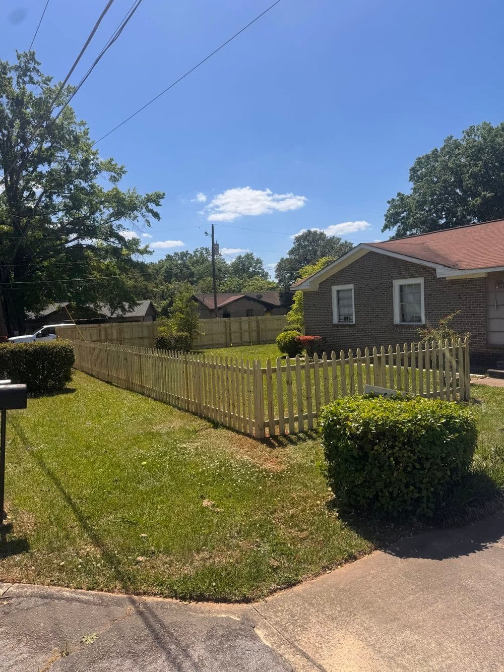 Green lawn with white picket fence surrounding a house under clear blue sky.