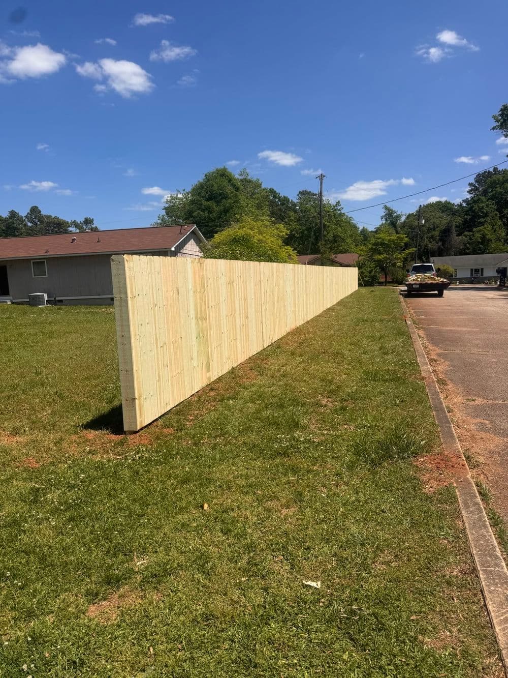New wooden fence lined on grassy area under blue sky with scattered clouds.