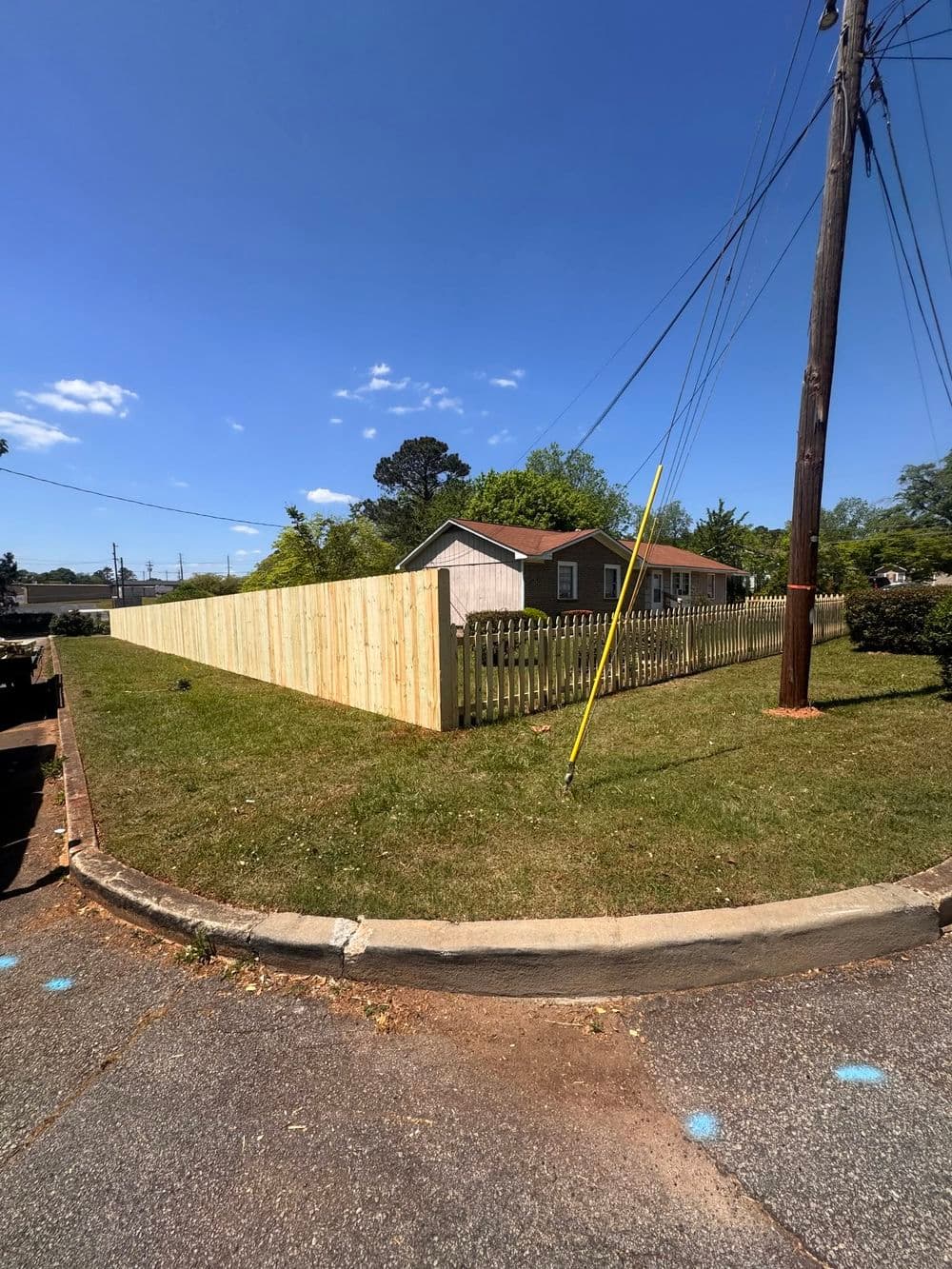 Wooden fence surrounds a residential yard under clear blue sky with utility poles nearby.