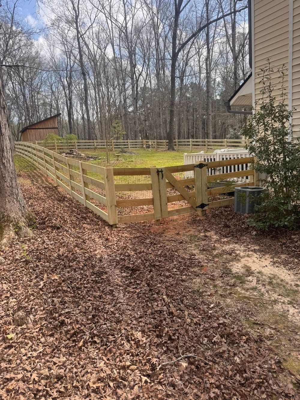 Wooden fence and gate leading into a yard surrounded by trees and fallen leaves.